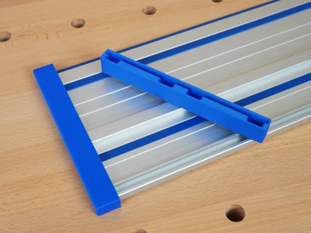 Blue PETG protective caps fitted over both ends of a Kreg ACS aluminum guide rail on a wood workbench