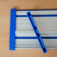 Blue PETG protective caps on Kreg ACS guide rail, one fitted on left end, one angled on rail surface showing slot design