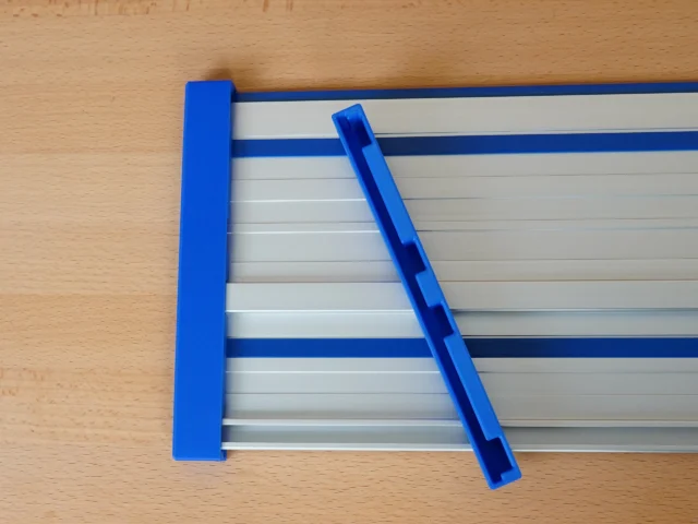 Blue PETG protective caps on Kreg ACS guide rail, one fitted on left end, one angled on rail surface showing slot design