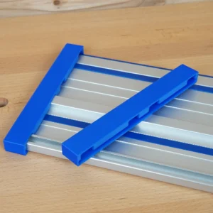 Two blue end caps resting on a Kreg ACS aluminum guide rail, showing their hollow channeled ends
