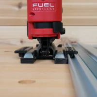 Red Milwaukee M12 Fuel jig saw mounted on black ToolCurve adapter seated on aluminum track rail, front view