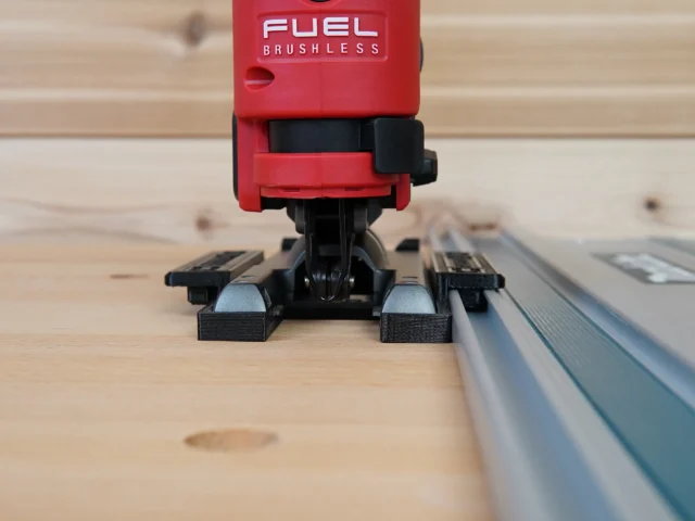 Red Milwaukee M12 Fuel jig saw mounted on black ToolCurve adapter seated on aluminum track rail, front view