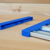 Two blue PETG protective caps, one empty and one fitted over a silver Kreg ACS aluminum guide rail