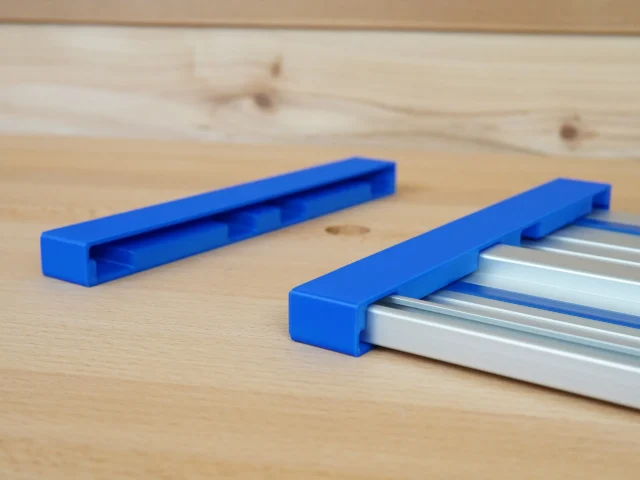 Two blue PETG protective caps, one empty and one fitted over a silver Kreg ACS aluminum guide rail