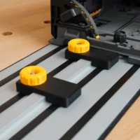 Two black limit stops with yellow knobs mounted on Dewalt guide rails, positioned on a wooden workbench