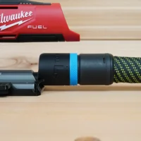 Black hose adapter with blue band attached to Milwaukee M12 Fuel Jig Saw dust port, connected to green and yellow braided hose