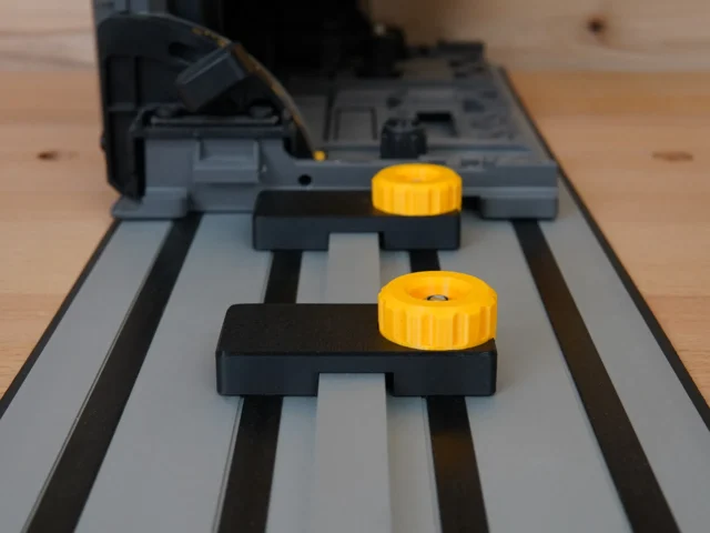 Two black limit stops with yellow knobs mounted on a Dewalt track saw guide rail, positioned at different points along the track