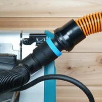 Black 1-1/4 inch hose adapter with blue band joining an orange vacuum hose to a Makita miter saw dust port