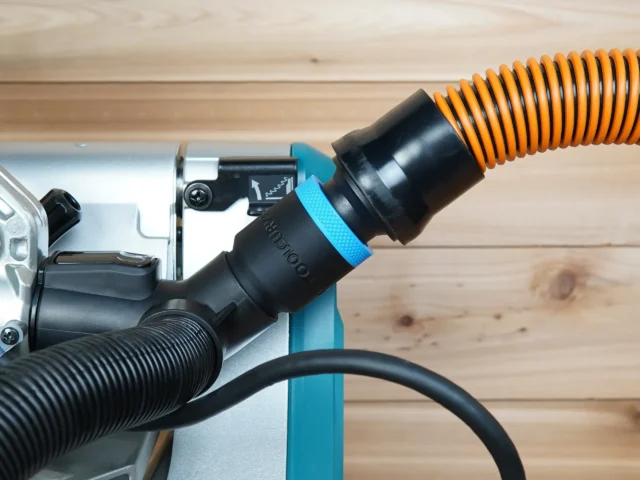 Black 1-1/4 inch hose adapter with blue band joining an orange vacuum hose to a Makita miter saw dust port