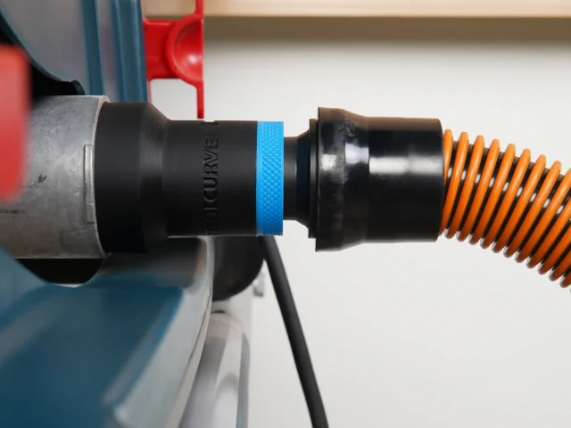 Black ToolCurve 1-1/4 inch hose adapter with blue band joining a Bosch table saw dust port to an orange vac hose