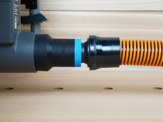 Black ToolCurve 1-1/4 inch hose adapter with blue band linking a Ryobi table saw dust port to an orange hose