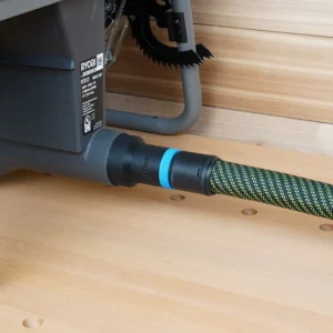 Black hose adapter with blue ring joining a braided vacuum hose to the rear dust port of a Ryobi RTS12 table saw