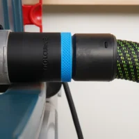 Black ToolCurve 36mm hose adapter with blue ring joining a green-striped hose to a Bosch table saw dust port