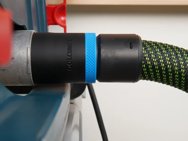 Black ToolCurve 36mm hose adapter with blue ring joining a green-striped hose to a Bosch table saw dust port