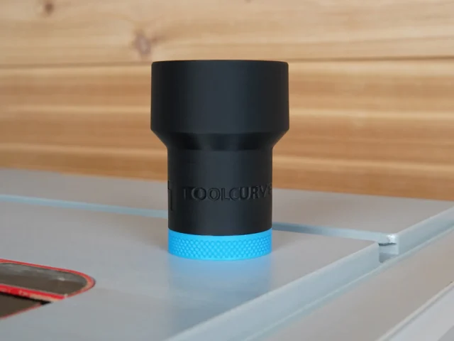 Black ToolCurve hose adapter with blue band, standing on aluminum track, wooden workbench in background