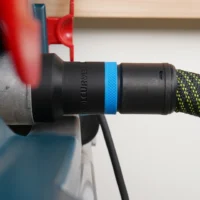 Black hose adapter with blue band attached to Bosch table saw dust port, connected to green and black braided hose