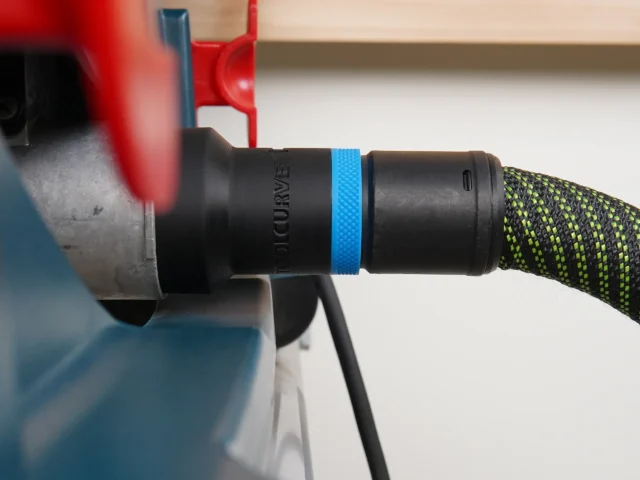 Black hose adapter with blue band attached to Bosch table saw dust port, connected to green and black braided hose