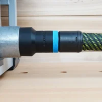 Black hose adapter with blue identification band attached to FLEX table saw dust port, connected to green and yellow braided hose