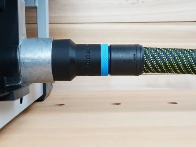 Black hose adapter with blue identification band attached to FLEX table saw dust port, connected to green and yellow braided hose