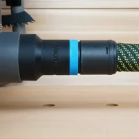 Black hose adapter with blue band attached to Ryobi table saw dust port, connected to green and yellow braided hose