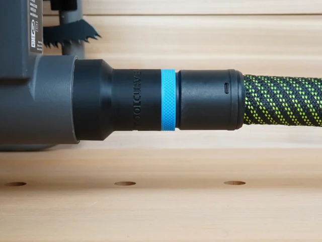 Black hose adapter with blue band attached to Ryobi table saw dust port, connected to green and yellow braided hose