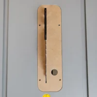 Tan MDF zero clearance insert for Bosch 4100 table saw, shown flat with vertical black slot and round hole for blade alignment, two mounting screw holes visible on each side