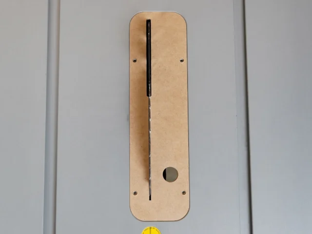 Tan MDF zero clearance insert for Bosch 4100 table saw, shown flat with vertical black slot and round hole for blade alignment, two mounting screw holes visible on each side