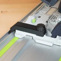 Black and white anti-tip guide with knurled adjustment knob mounted on Festool TS 55 track saw rail, shown at an angle over wooden surface