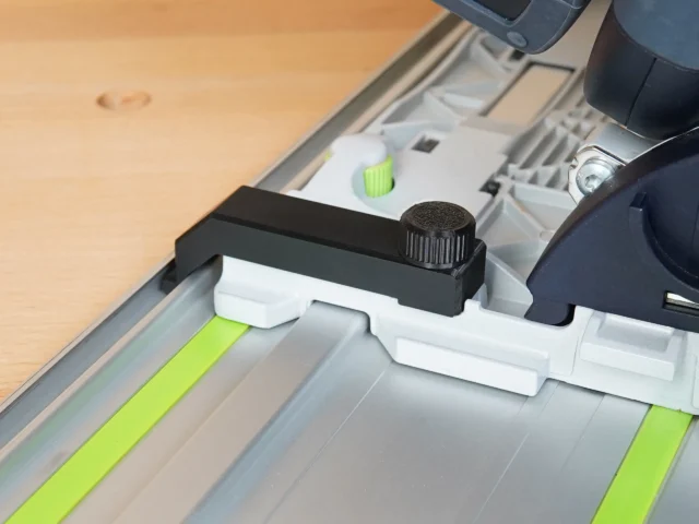 Black and white anti-tip guide with knurled adjustment knob mounted on Festool TS 55 track saw rail, shown at an angle over wooden surface