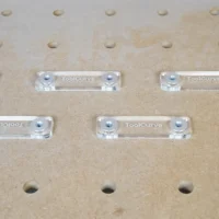 Six clear acrylic fence stops with threaded holes and aluminum bench dogs, arranged on a 20mm pegboard workbench system