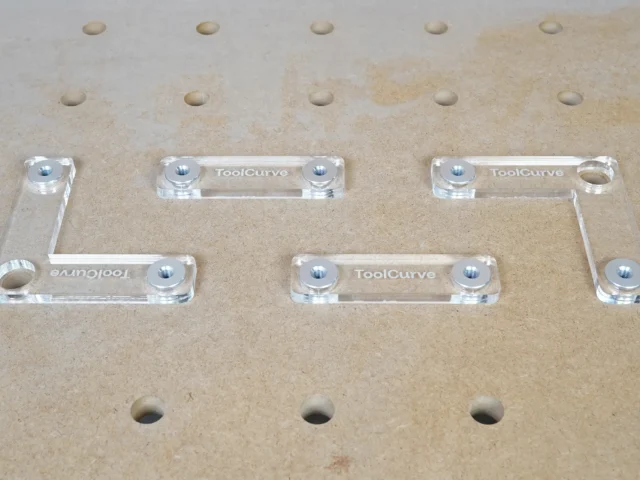 Six clear acrylic fence stops with threaded holes and aluminum bench dogs, arranged on a 20mm pegboard workbench system