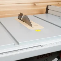 Beige MDF zero clearance insert with stainless offset screws installed on a Bosch 4100 table saw, holding a saw blade upright