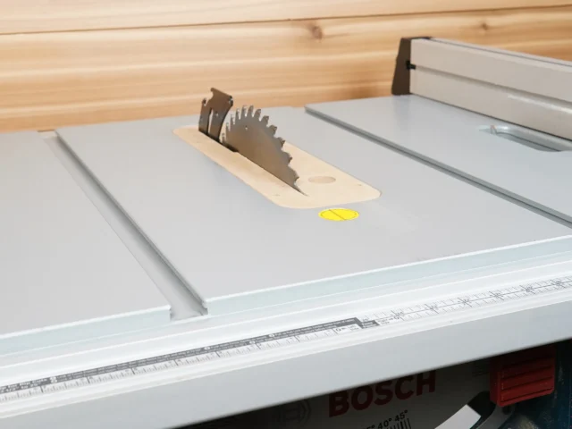 Beige MDF zero clearance insert with stainless offset screws installed on a Bosch 4100 table saw, holding a saw blade upright