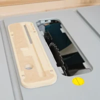 Light wood zero clearance insert next to Bosch 4100 table saw's factory insert, showing the recessed blade opening and mounting holes