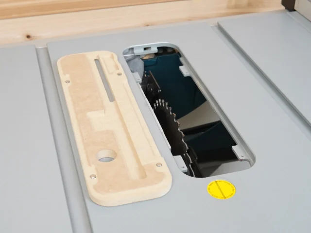 Light wood zero clearance insert next to Bosch 4100 table saw's factory insert, showing the recessed blade opening and mounting holes