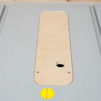 Beige MDF zero clearance insert for Bosch 4100 table saw, seated in aluminum slot with center oval opening and mounting holes visible