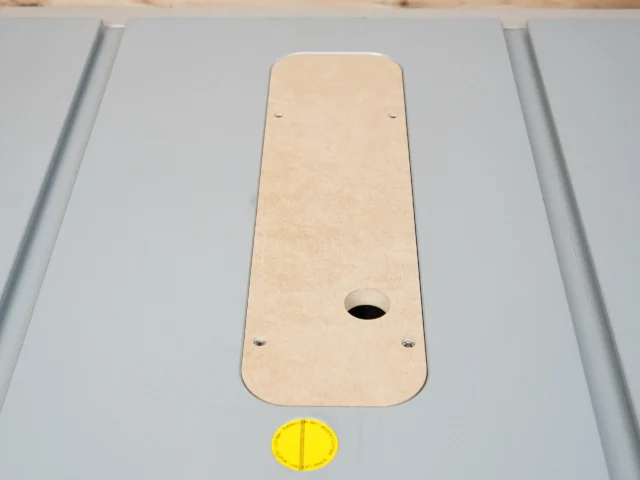 Beige MDF zero clearance insert for Bosch 4100 table saw, seated in aluminum slot with center oval opening and mounting holes visible