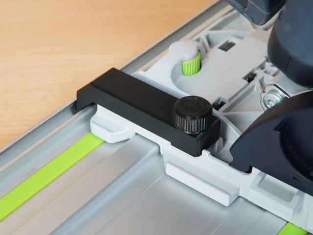 Black anti-tip guide installed on Festool TS 55 track saw rail, showing knurled adjustment knob and mounting bracket