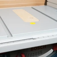 Cream MDF zero clearance insert seated in Bosch 4100 table saw, with yellow reference dot and wooden test piece visible on surface