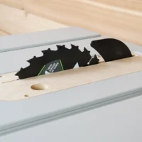 Zero clearance insert for FLEX table saw installed in saw slot, showing MDF base with mounting holes and two saw blades positioned above