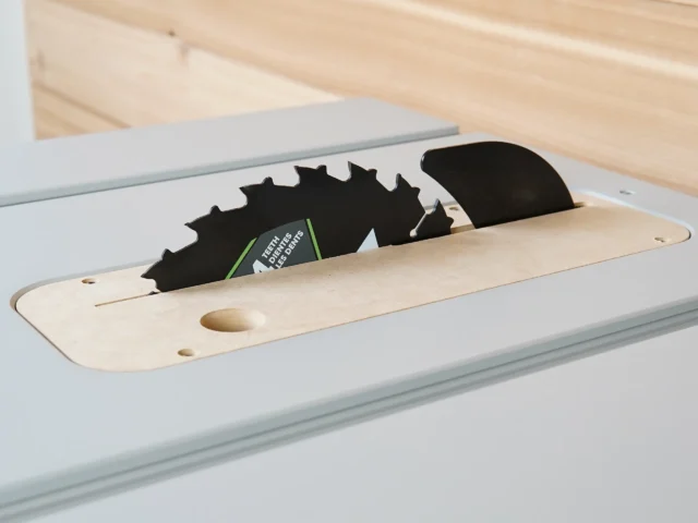 Zero clearance insert for FLEX table saw installed in saw slot, showing MDF base with mounting holes and two saw blades positioned above