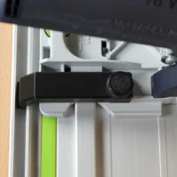 Anti-tip guide mounted on Festool TS 55 track saw, showing black bracket with adjustment knob attached to the saw's rail system