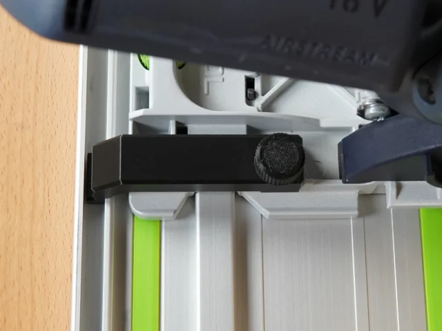 Anti-tip guide mounted on Festool TS 55 track saw, showing black bracket with adjustment knob attached to the saw's rail system