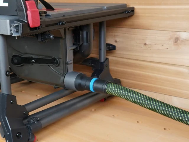 Hose adapter with blue band attached to SKIL table saw's rear dust port, connected to green and black hose