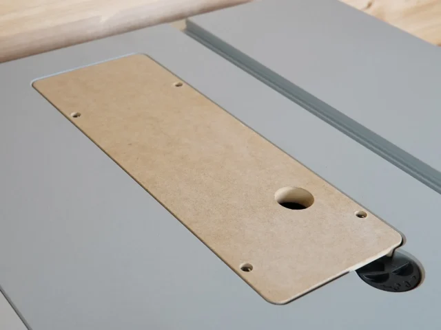 Tan MDF zero clearance insert with central blade slot and mounting holes, positioned on a Bosch table saw next to gray aluminum fence