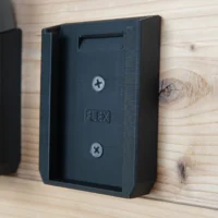 Black plastic wall-mount battery holder for FLEX 24v batteries, shown attached to wood with two screw holes visible