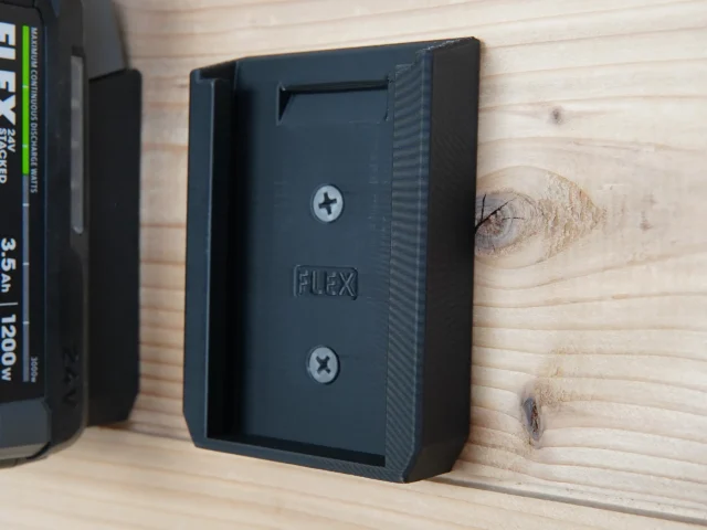 Black plastic wall-mount battery holder for FLEX 24v batteries, shown attached to wood with two screw holes visible