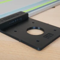 Black plastic adapter plate with central circular opening, mounted on a Festool track saw rail with alignment markings visible
