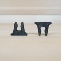 Two black 3D-printed stop blocks shown side by side, displaying the U-shaped clamp slot design from different angles