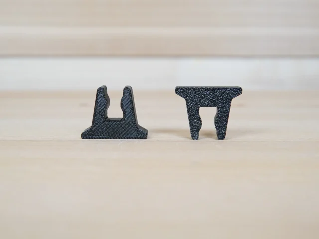 Two black 3D-printed stop blocks shown side by side, displaying the U-shaped clamp slot design from different angles